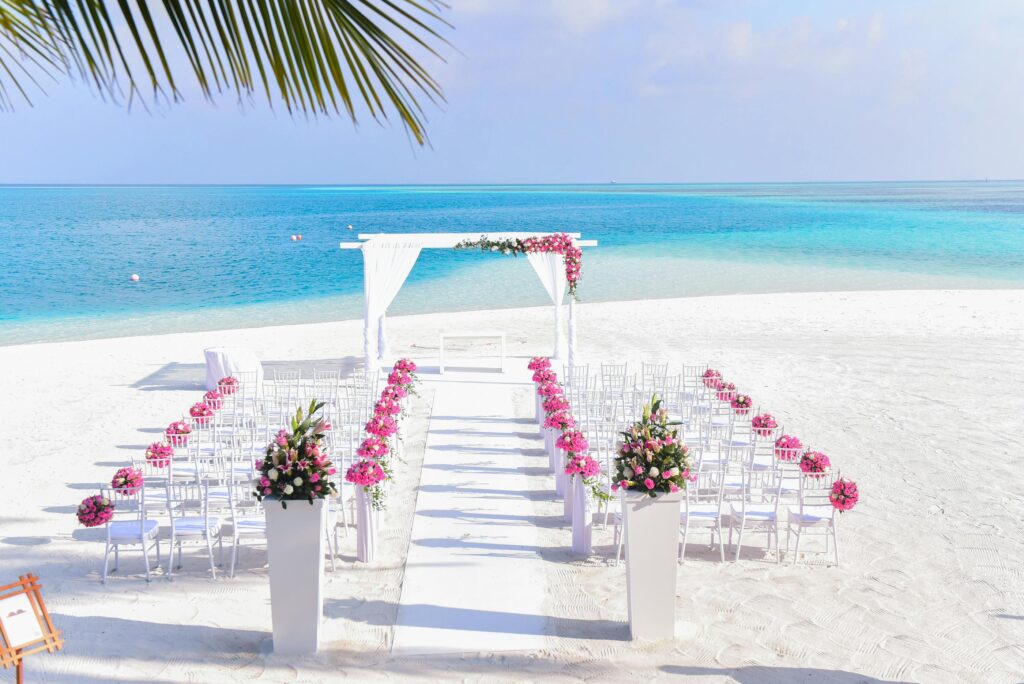 Exquisite beach wedding setup featuring pink floral decor, ocean view, and white chairs on a sunny day.